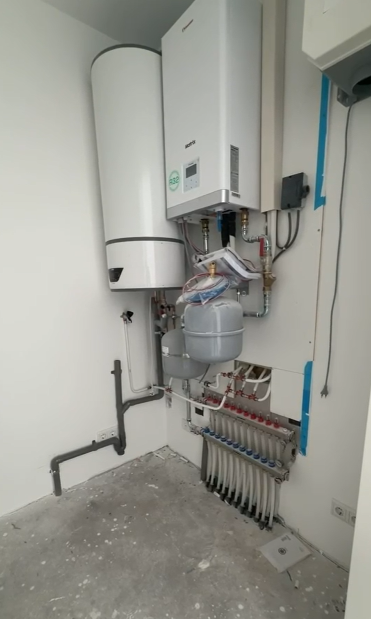 Warmtepompunit met boiler en vloerverwarmingsverdeler in de technische ruimte van een appartement in Groenlo
